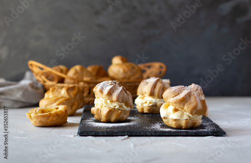 Cream puffs with whipped cream is a classic French dessert also called choux pastry, on black slate board, dusted with sugar powder.