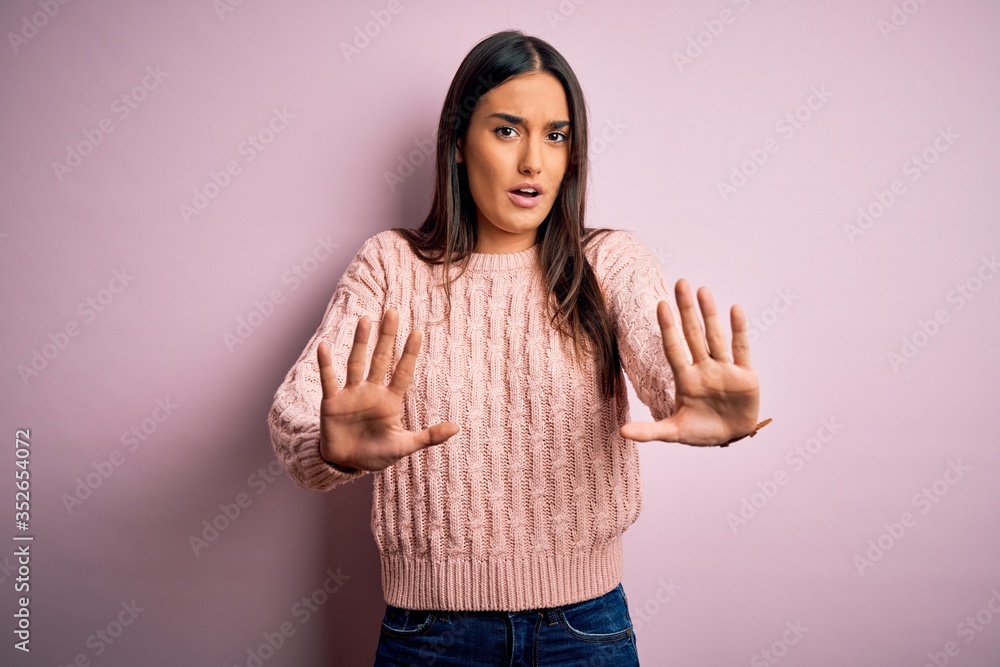 Young beautiful brunette woman wearing casual sweater over isolated pink background doing stop gesture with hands palms, angry and frustration expression Young beautiful brunette woman wearing casual sweater over isolated pink background doing stop gesture with hands palms, angry and frustration expression