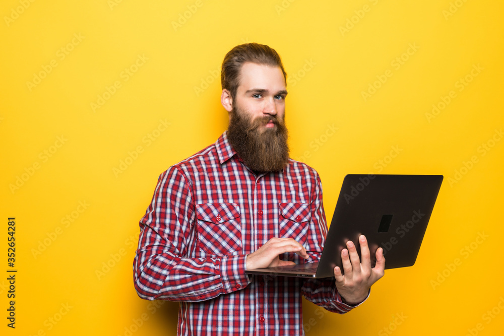 Young bearded man with laptop on yellow background Young bearded man with laptop on yellow background