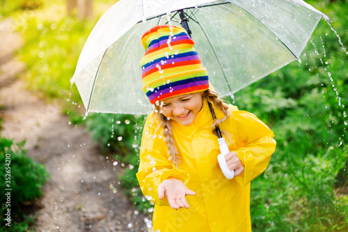 little Blonde Girl Smiles Jumps on Puddles in Spring in yellow raincoat and rubber boots with umbrella photo