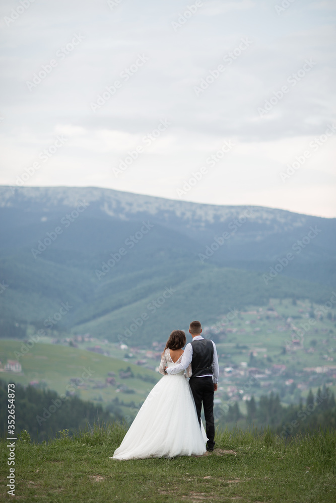 Wedding. The bride and groom running through the mountain slope. After wedding session. The guy in the white shirt and waistcoat, and a girl in white dress walk on the green glade in the mountains Wedding. The bride and groom running through the mountain slope. After wedding session. The guy in the white shirt and waistcoat, and a girl in white dress walk on the green glade in the mountains