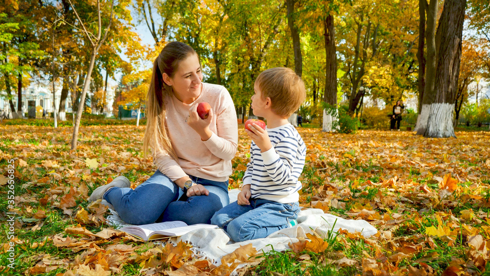 Portrait of young smiling mother with little son having picnic on blanket at autumn park Portrait of young smiling mother with little son having picnic on blanket at autumn park