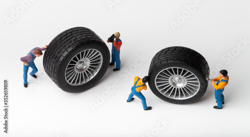 The concept of the workshop tire fitting. Miniature mechanics repairing toy car wheel, close up.