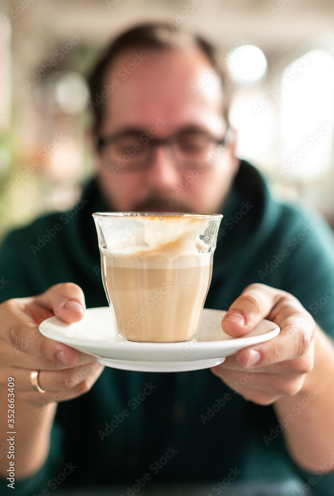 Vertical frame with real malepperson with glasses closed his eyes holds in front of his face aucer with cup of coffee from which several sips were made. Mental health and self care, concept Vertical frame with real malepperson with glasses closed his eyes holds in front of his face aucer with cup of coffee from which several sips were made. Mental health and self care, concept