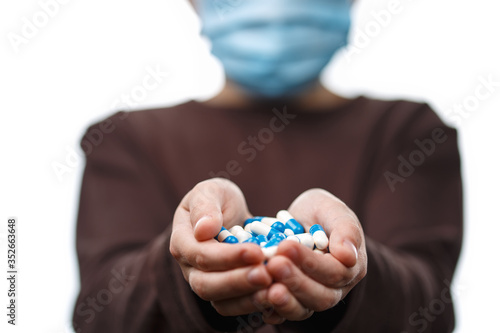 Child in medical mask holds handful of pills.