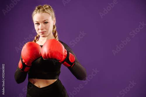 Sports young woman wearing boxing gloves on color background