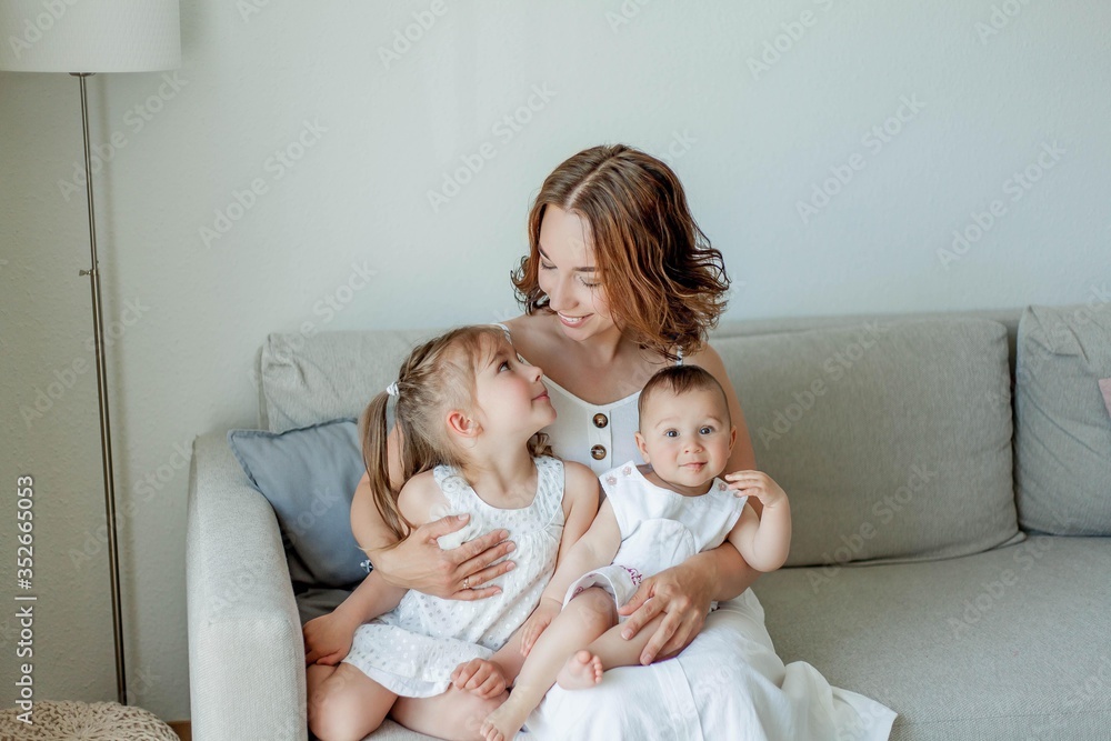 Young beautiful mother Holds her little daughters in her arms. Home comfort. Mothers Day. Young beautiful mother Holds her little daughters in her arms. Home comfort. Mothers Day.