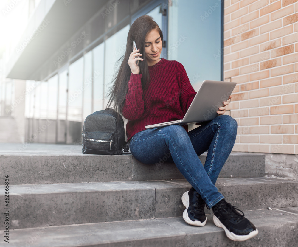 Young woman sit on urban stairs and work with laptop on the street