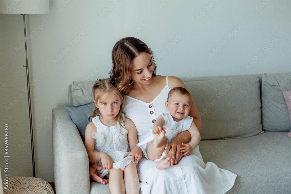 Young beautiful mother Holds her little daughters in her arms. Home comfort. Mothers Day. Young beautiful mother Holds her little daughters in her arms. Home comfort. Mothers Day.
