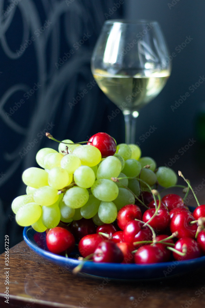 Cherry, bunch of grape, white wine glass on wooden table