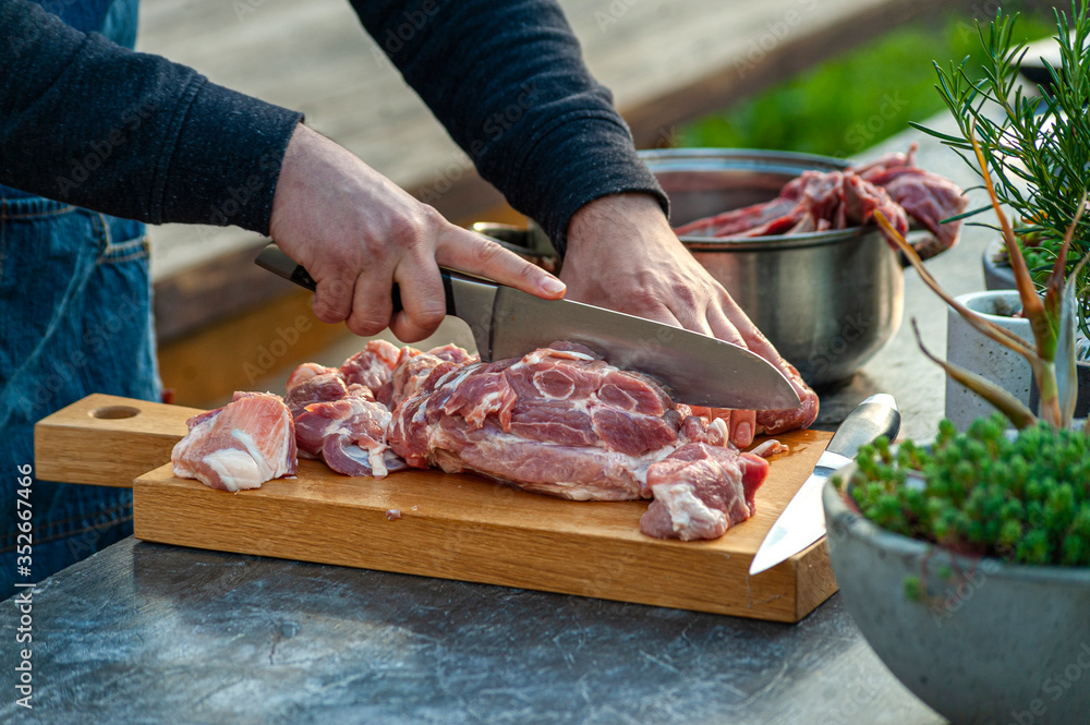 Man chef slicing big piece of pork meat on wooden cutting board