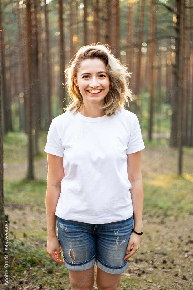 Three quarter crop portrait of young attractive caucasian etnicity womanstanding in the middle of pine forest and smiling liikong right into the camera. Safe, socially distanced outdoor walks Three quarter crop portrait of young attractive caucasian etnicity womanstanding in the middle of pine forest and smiling liikong right into the camera. Safe, socially distanced outdoor walks