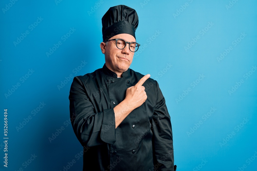Middle age handsome grey-haired chef man wearing cooker uniform and hat Pointing with hand finger to the side showing advertisement, serious and calm face Middle age handsome grey-haired chef man wearing cooker uniform and hat Pointing with hand finger to the side showing advertisement, serious and calm face