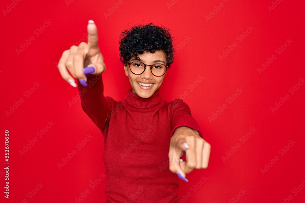 Young beautiful african american afro woman wearing turtleneck sweater and glasses pointing to you and the camera with fingers, smiling positive and cheerful Young beautiful african american afro woman wearing turtleneck sweater and glasses pointing to you and the camera with fingers, smiling positive and cheerful