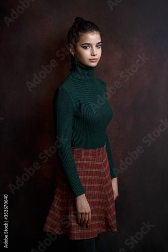 a girl in a green sweater and skirt on a dark background