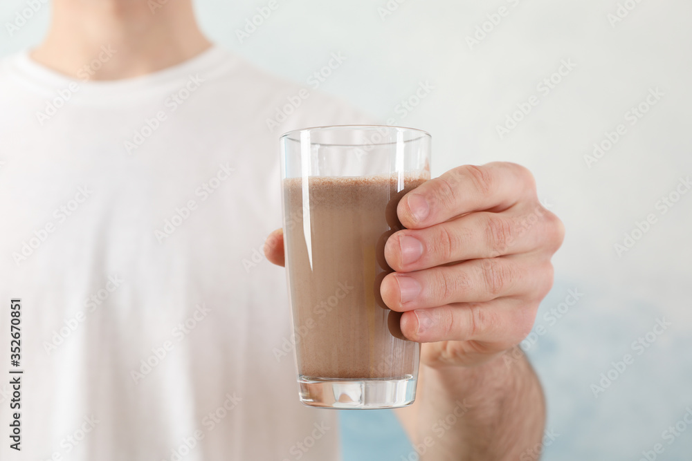 Young man holds glass of chocolate milkshake against blue background Young man holds glass of chocolate milkshake against blue background