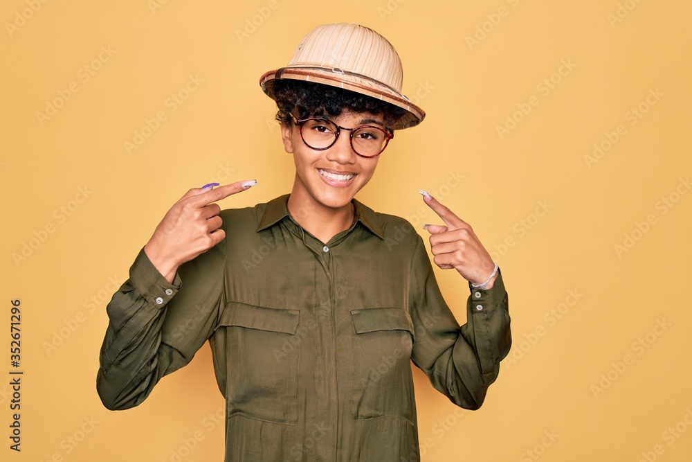 Young beautiful african american tourist woman wearing glasses and explorer hat smiling cheerful showing and pointing with fingers teeth and mouth. Dental health concept. Young beautiful african american tourist woman wearing glasses and explorer hat smiling cheerful showing and pointing with fingers teeth and mouth. Dental health concept.