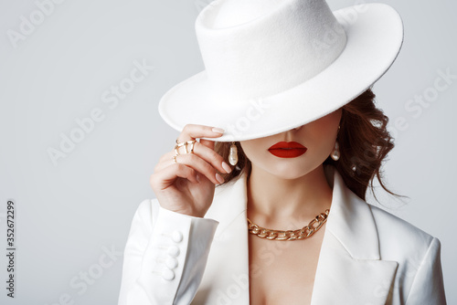 Luxury beautiful fashionable woman wearing stylish accessories: earrings, rings, chain, white hat. Hidden eyes. Female fashion, beauty, advertising concept. Close up studio portrait. Copy, empty space