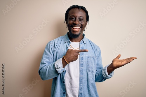 Fényképezés Young handsome african american man wearing casual denim shirt over white background amazed and smiling to the camera while presenting with hand and pointing with finger