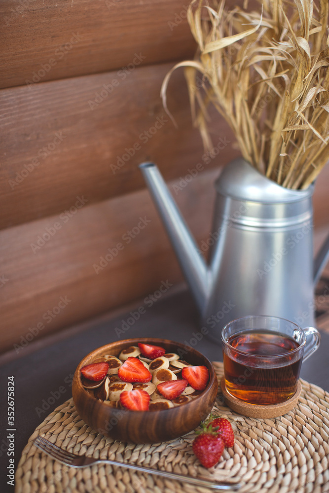 Fototapeta premium Tiny pancake cereal mini pancakes in a wooden bowl with strawberries on a wooden background. Top view. Copy space