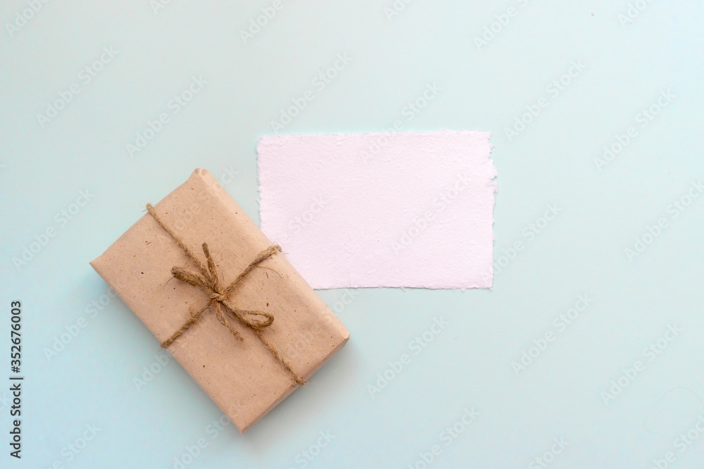 Gift box with kraft paper and a sheet of paper for text on a light blue background. Flat lay for father's day concept. Gift box with kraft paper and a sheet of paper for text on a light blue background. Flat lay for father's day concept.