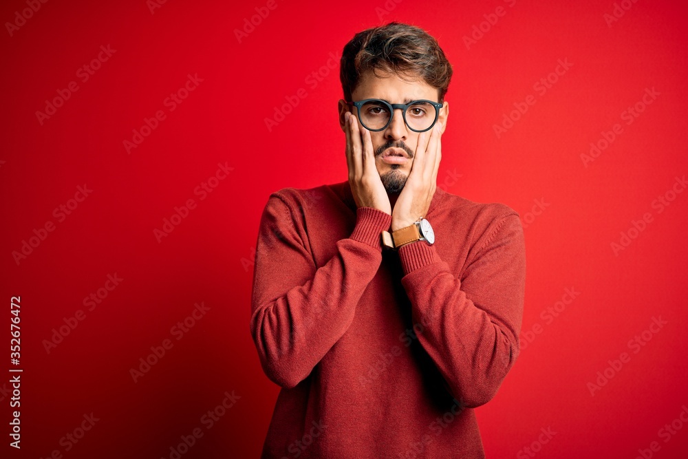 Young handsome man with beard wearing glasses and sweater standing over red background Tired hands covering face, depression and sadness, upset and irritated for problem Young handsome man with beard wearing glasses and sweater standing over red background Tired hands covering face, depression and sadness, upset and irritated for problem