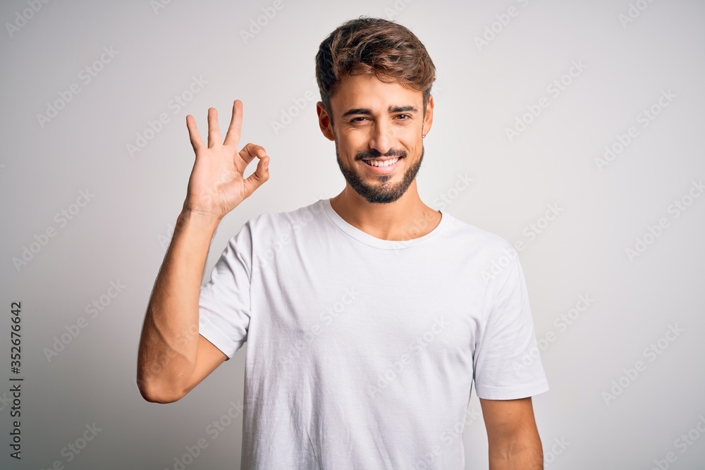Young handsome man with beard wearing casual t-shirt standing over white background smiling positive doing ok sign with hand and fingers. Successful expression. Young handsome man with beard wearing casual t-shirt standing over white background smiling positive doing ok sign with hand and fingers. Successful expression.