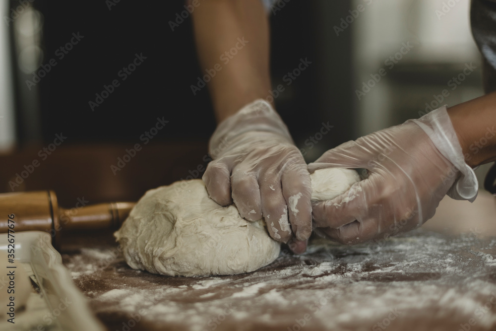 Hands of a woman making dough with plastic gloves on the table