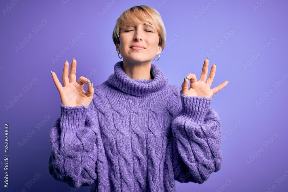 Young blonde woman with short hair wearing winter turtleneck sweater over purple background relaxed and smiling with eyes closed doing meditation gesture with fingers. Yoga concept. Young blonde woman with short hair wearing winter turtleneck sweater over purple background relaxed and smiling with eyes closed doing meditation gesture with fingers. Yoga concept.