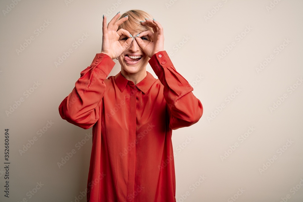 Young beautiful business blonde woman with short hair standing over isolated background doing ok gesture like binoculars sticking tongue out, eyes looking through fingers. Crazy expression. Young beautiful business blonde woman with short hair standing over isolated background doing ok gesture like binoculars sticking tongue out, eyes looking through fingers. Crazy expression.
