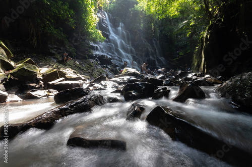 sun shines through the jungle at waterfall in bali indonesia