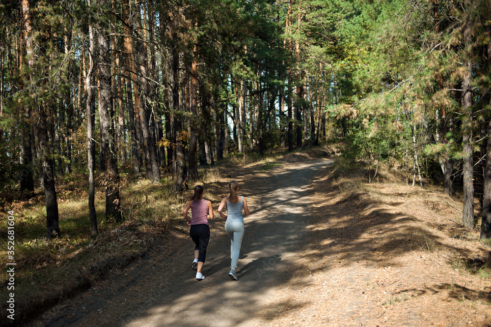 Two girls of the athlete perform a run in the morning in the sunny forest