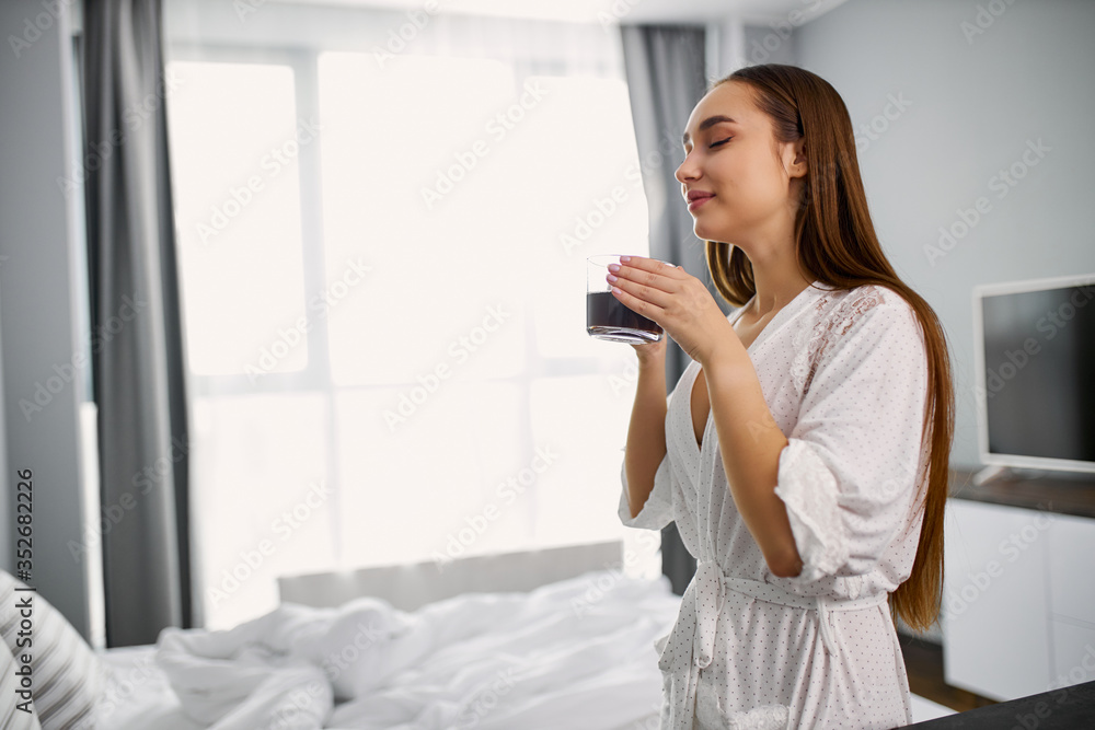 attractive young caucasian lady is enjoying smell of hot coffee, woman inhales aroma of coffee in bedroom attractive young caucasian lady is enjoying smell of hot coffee, woman inhales aroma of coffee in bedroom