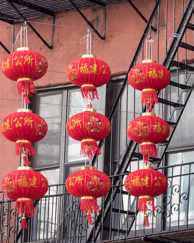 Fotografie 3 rows of Asian, bright, red paper lanterns hanging near a fire escape by apartments in a city
