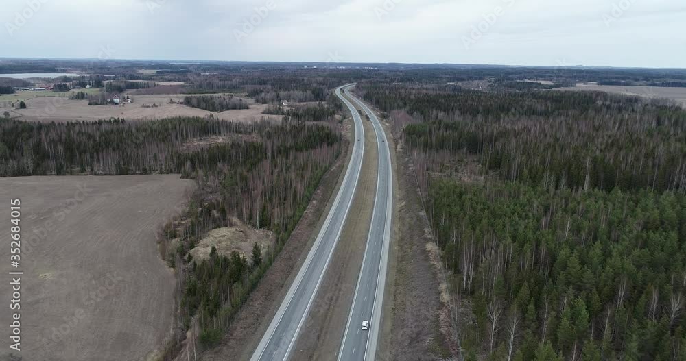Aerial shot moving forward over countryside highway with moving cars at summer cloudy day surrounded by field and trees top view.Business Transportation, Trucking Industry. Aerial shot moving forward over countryside highway with moving cars at summer cloudy day surrounded by field and trees top view.Business Transportation, Trucking Industry.