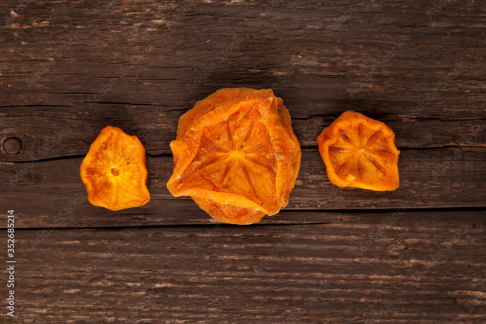 Dried persimmons. Bright orange slices on a brown wooden background. Useful sweets. Ingredients for fruit tea or punch. Selective focus