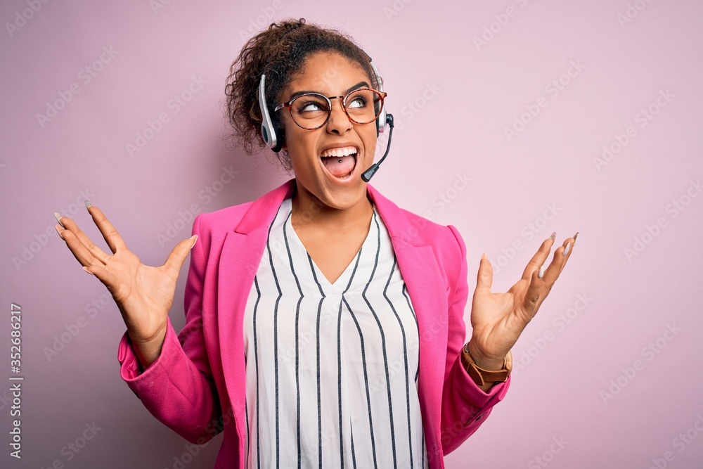 Young african american call center agent girl wearing glasses working using headset crazy and mad shouting and yelling with aggressive expression and arms raised. Frustration concept. Young african american call center agent girl wearing glasses working using headset crazy and mad shouting and yelling with aggressive expression and arms raised. Frustration concept.