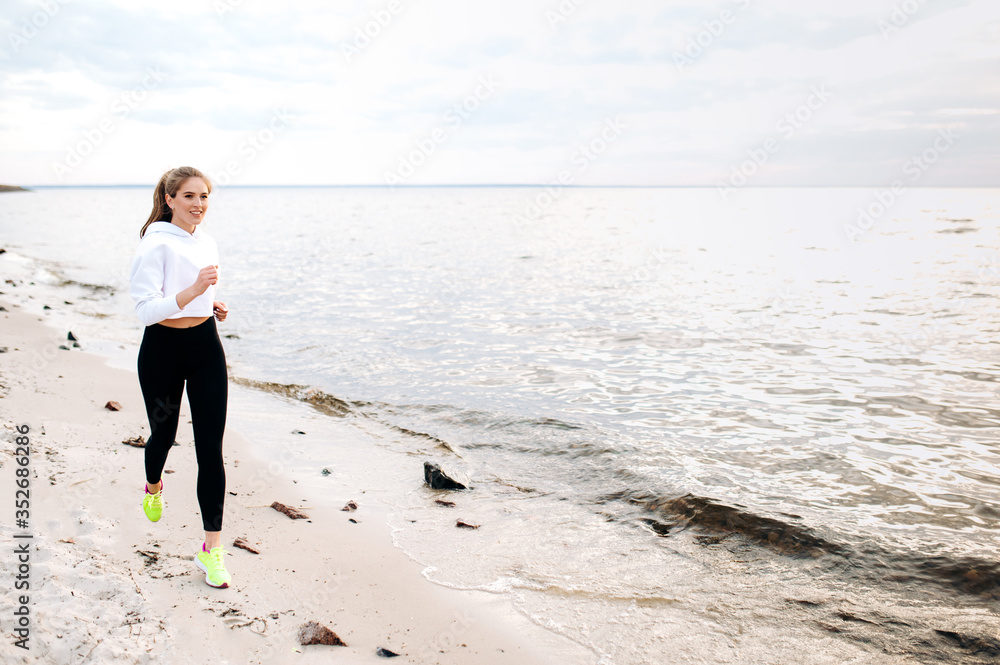 Jogging by the sea. A beautiful young girl dressed in stylish sportswear is jogging on the seashore. Keeping yourself in a good shape Jogging by the sea. A beautiful young girl dressed in stylish sportswear is jogging on the seashore. Keeping yourself in a good shape