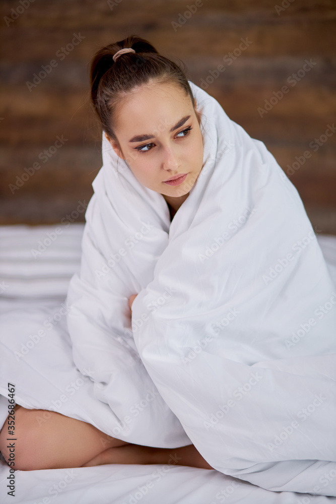 young beautiful girl is cold at home, she is wrapped in blanket. woman on bed, looks side young beautiful girl is cold at home, she is wrapped in blanket. woman on bed, looks side