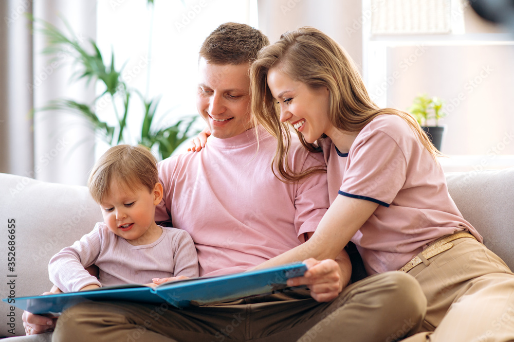 Family leisure at home. Young happy parents read a children's book with their adorable little son, sitting at home on the couch Family leisure at home. Young happy parents read a children's book with their adorable little son, sitting at home on the couch