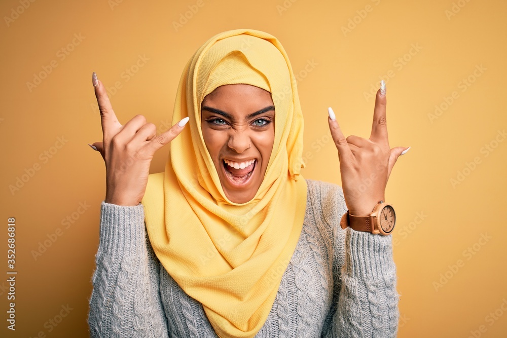 Φωτογραφία Young beautiful african american girl wearing muslim hijab over isolated yellow background shouting with crazy expression doing rock symbol with hands up