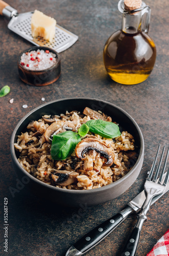 Traditional italian risotto with mushrooms and parmesan cheese on a dark bowl on a black table.