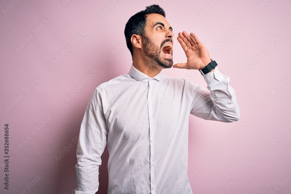 Young handsome man with beard wearing casual shirt standing over pink background shouting and screaming loud to side with hand on mouth. Communication concept. Young handsome man with beard wearing casual shirt standing over pink background shouting and screaming loud to side with hand on mouth. Communication concept.