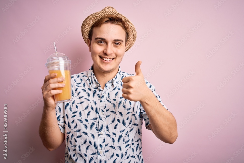 Young handsome redhead man on vacation drinking glass of healthy orange juice Smiling happy and positive, thumb up doing excellent and approval sign Young handsome redhead man on vacation drinking glass of healthy orange juice Smiling happy and positive, thumb up doing excellent and approval sign