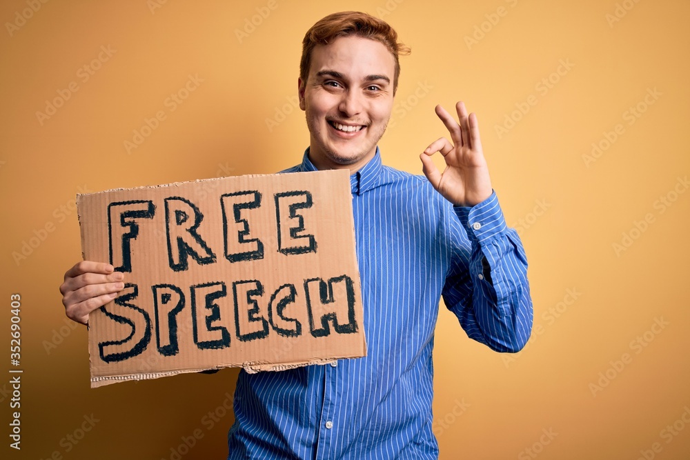 Young handsome redhead man asking for freedom holding banner with free speech message doing ok sign with fingers, smiling friendly gesturing excellent symbol Young handsome redhead man asking for freedom holding banner with free speech message doing ok sign with fingers, smiling friendly gesturing excellent symbol