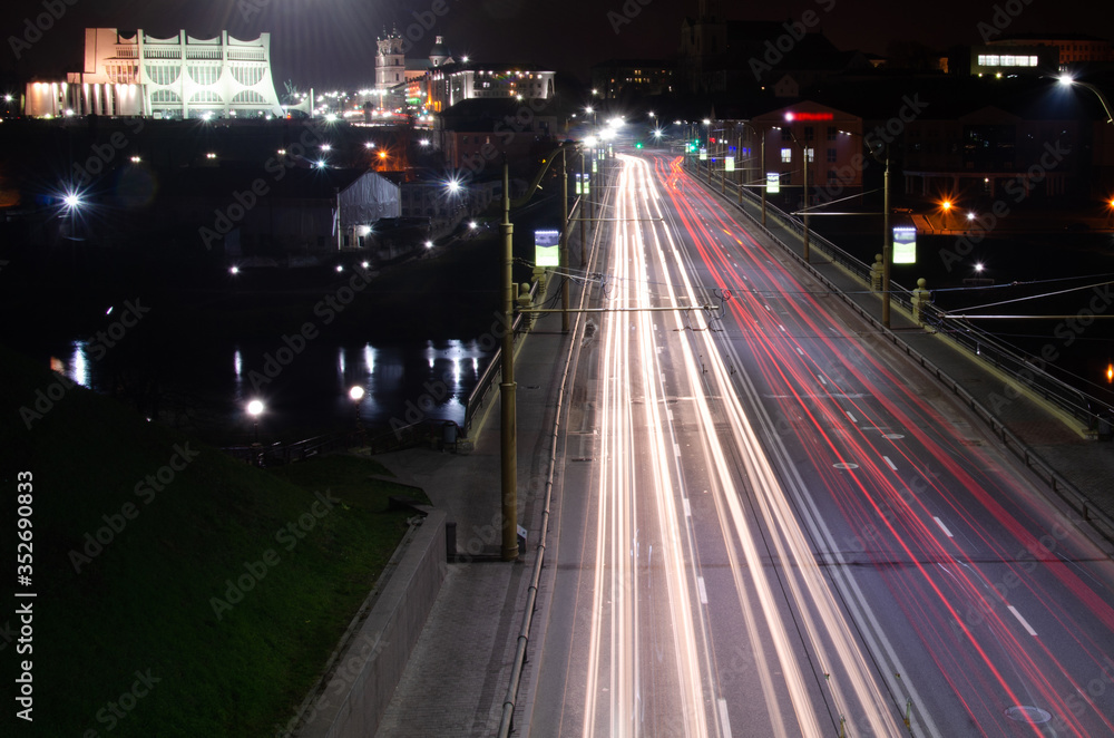 Night city. The light trails on the street. Slow shutter speed photo. A long bridge across the river leads to the big city. A busy expressway in the town center.