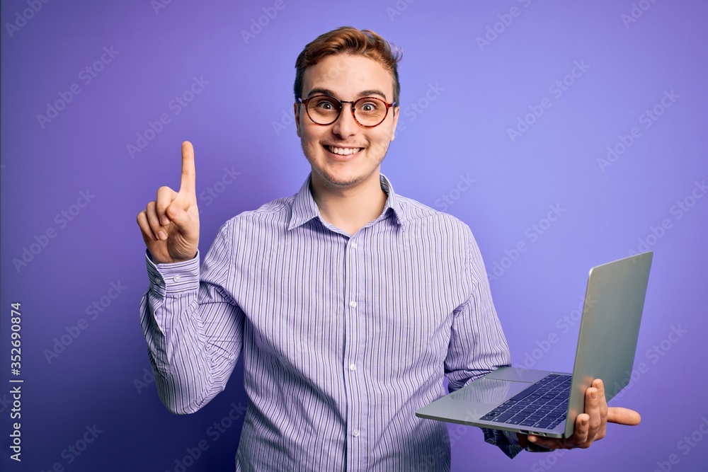 Young handsome redhead businessman working using laptop over purple background surprised with an idea or question pointing finger with happy face, number one Young handsome redhead businessman working using laptop over purple background surprised with an idea or question pointing finger with happy face, number one