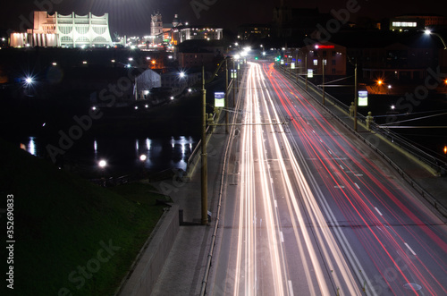 Night city. The light trails on the street. Slow shutter speed photo. A long bridge across the river leads to the big city. A busy expressway in the town center.