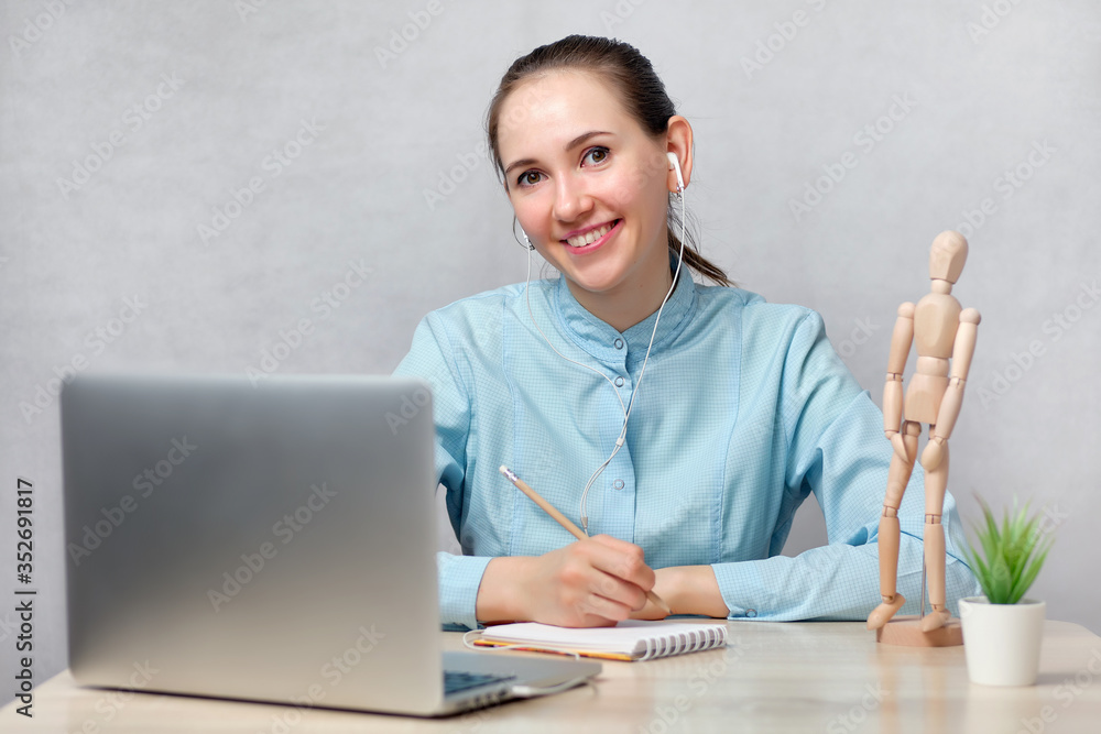 Girl doctor student sitting at a table with a laptop in headphones and smiling looking at the camera Girl doctor student sitting at a table with a laptop in headphones and smiling looking at the camera