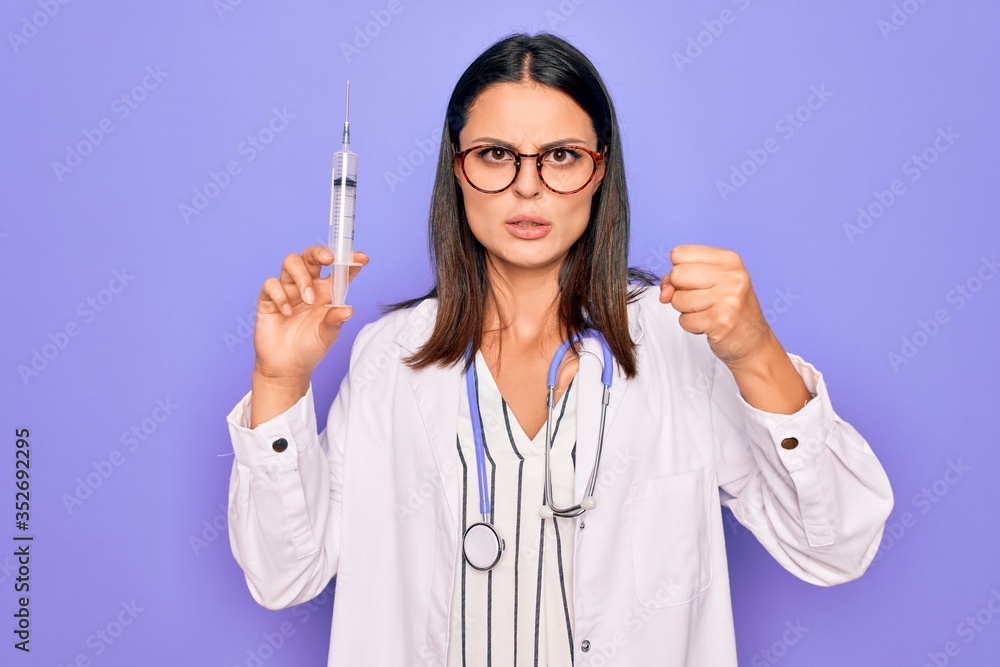 Young beautiful brunette doctor woman wearing stethoscope holding syringe vaccination annoyed and frustrated shouting with anger, yelling crazy with anger and hand raised Young beautiful brunette doctor woman wearing stethoscope holding syringe vaccination annoyed and frustrated shouting with anger, yelling crazy with anger and hand raised